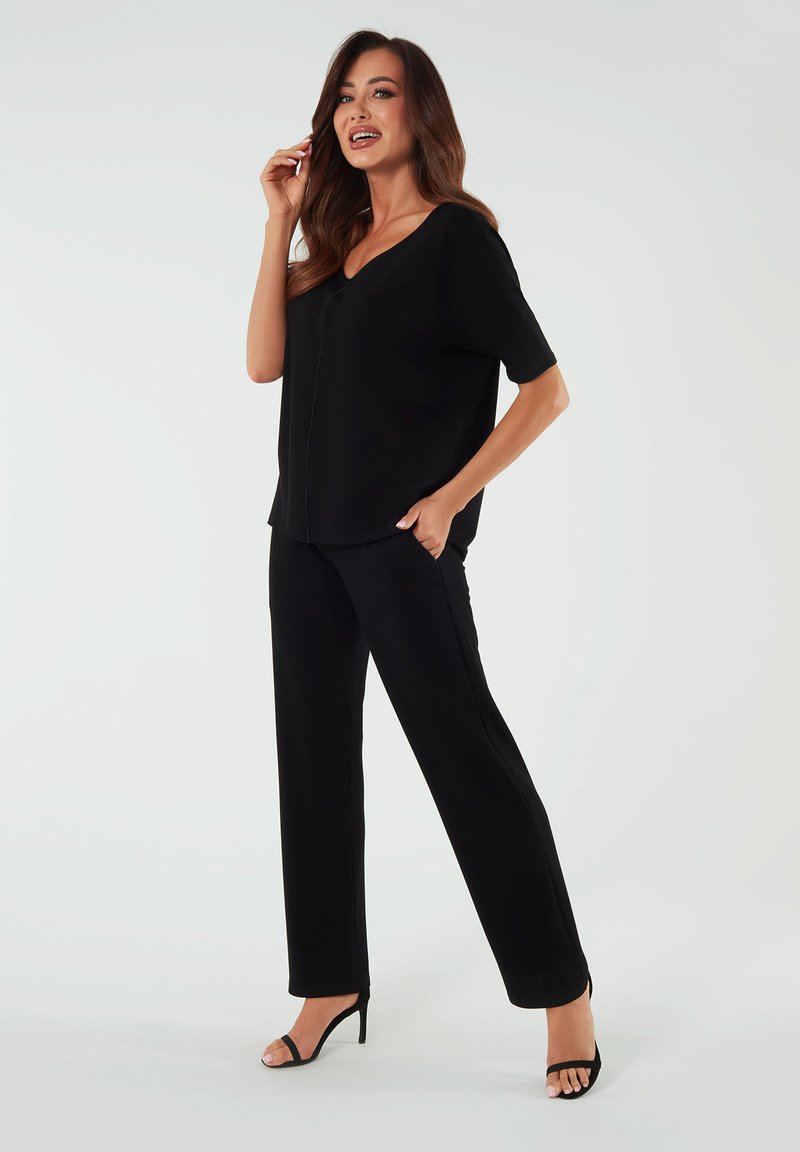 Czarna, luźna bluzka z krótkimi rękawami, dekoltem w serek oraz dopasowanym czarnym spodniami. Charakteryzuje się eleganckim krojem i miękką teksturą.