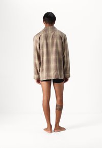 Brun rutigt oversized skjorta med långa ärmar, lättviktsmaterial och rak skärning, bärs över svarta shorts.