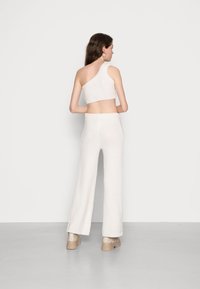 Top cropped branco tricotado com design de um ombro, combinado com calças largas a condizer. Apresenta um acabamento texturizado e cintura elástica.