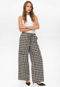 Pantalon large à carreaux en beige et bleu marine, avec une taille à cordon de serrage et des poches latérales. Le tissu a une apparence texturée et tissée.