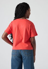 Camiseta de algodón roja con un corte relajado y mangas cortas, combinada con unos vaqueros de mezclilla azules que presentan un diseño clásico de bolsillo trasero.