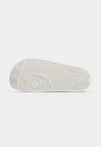 Semelle de chaussure en caoutchouc blanc avec des motifs de bande de roulement circulaires, hexagonaux et en chevron, montrée par le dessous sur un fond uni.