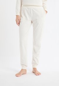 Jasnokremowe spodnie dresowe z miękkiego materiału z wzorem w gwiazdki. Posiadają elastyczną talię i ściągacze dla dopasowania.