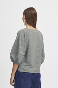 Haut bleu clair à motifs en losanges, avec de larges manches et un ourlet droit. Le tissu a une texture apparente.