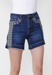 Shorts en denim bleu foncé avec broderies florales sur les côtés, ourlet effiloché et design traditionnel à cinq poches.