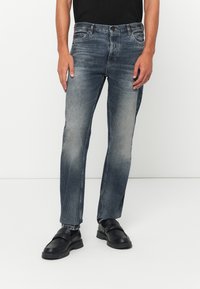 Modré džíny z denimu s vybledlým odstínem, designem s pěti kapsami, se zipem a rovnýma nohavicema. Nosené s černými koženými nazouvacími botami.