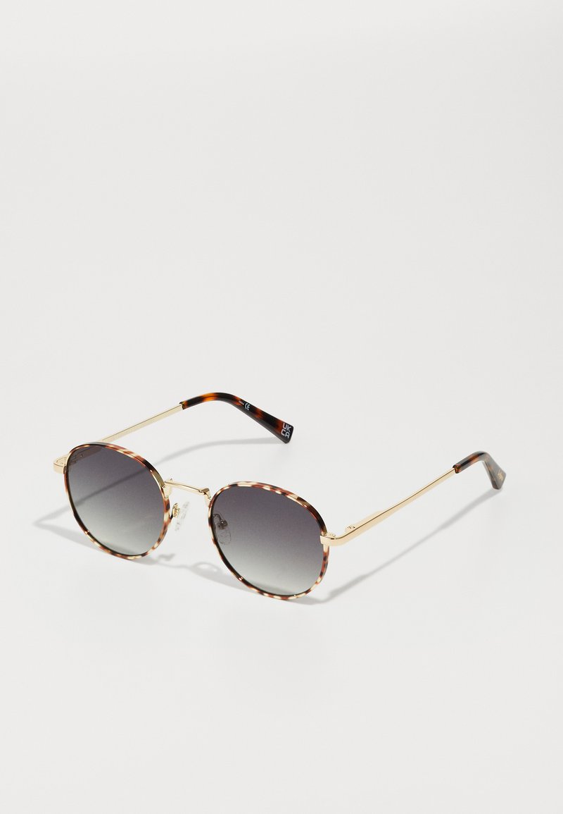 Óculos de sol redondos com lentes cinzentas em degradê, armações com padrão de tartaruga e braços em metal dourado. Possui almofadas nasais transparentes e detalhes nos templos.