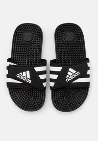 Czarne klapki Adidas z trzema białymi paskami, gumowa cholewka, teksturowana wkładka oraz miękki pasek dla komfortu. Podeszwa w kropki.