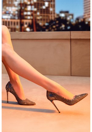 Des chaussures à talons hauts avec une base métallique recouverte de strass noirs, un design à bout pointu et un talon aiguille fin.