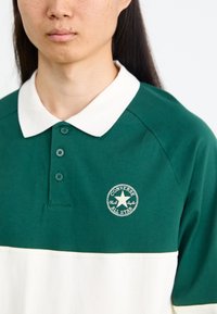Polo verde y blanco con un cuello blanco en contraste, tapeta de tres botones y un logo bordado "Converse All Star" en el pecho.