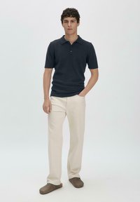 Navy polo shirt with short sleeves, two buttons, fitted design; paired with beige straight-leg trousers and brown slip-on shoes.