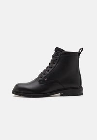 Bottine en cuir noir avec tige texturée, bout rond et laçage à l'avant. Présente une languette et un discret logo sur le côté.