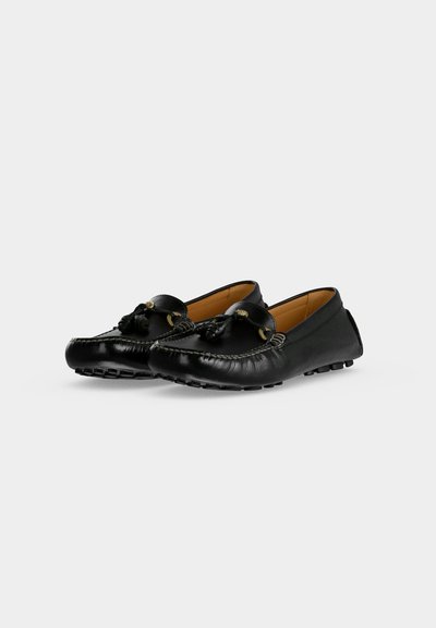 Paire de mocassins en cuir noir avec détail à pompon, bords cousus et semelles en caoutchouc à picots, présentée sur fond blanc.