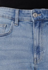 Jeanși din denim albastru deschis, cu talie standard, închidere cu nasture metalic, bucle pentru curea și buzunare frontale. Textură netedă, cu o estompare minimă.