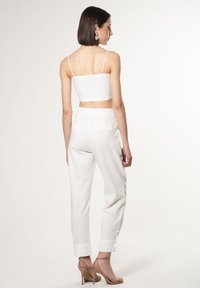 Witte crop top met dunne bandjes, gecombineerd met witte tapered broeken met zakken en omgeslagen boorden, gedragen met naaktkleurige hoge hakken.