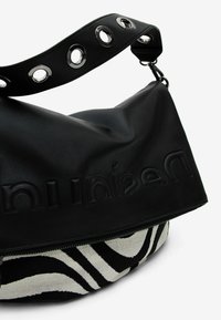 Mustakynäinen nahkalaukku, jossa on tekstuurilla varustettu läppä ja kohokuvioitu brändimerkintä. Zebraprinttipohja, jossa on vetoketju ja pyöreä metalliosa hihnassa.