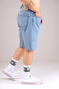 Denim shorts in light blue, featuring a relaxed fit, five pockets, and copper rivets. Paired with white sneakers and crew socks with black text.
