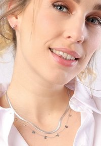 Zilveren gelaagde kettingen hebben een gladde slangeketting en een pendants met de letters "FOREVER." Draag het op een blote hals, in combinatie met een wit shirt.