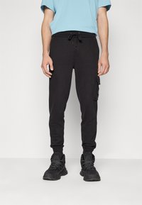 Svarta joggingbyxor med dragsko i midjan och sidofickor, tillverkade av mjukt material, med avsmalnande ben och ribbade muddkanter.