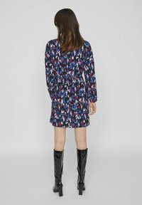 Vestido con estampado floral en azul marino, con tonalidades de azul, rosa y rojo. Manga larga, cintura con lazo y combinado con botas de charol negras hasta la rodilla.