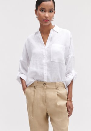 Weißes Leinenhemd mit Knöpfen und Brusttasche, hochgekrempelte Ärmel, kombiniert mit beigefarbenen High-Waist-Hosen mit doppelten Knöpfen.