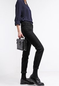 Jeans negros con los puños enrollados, combinados con una camisa de botones azul marino. Los accesorios incluyen un pequeño bolso negro y zapatos de piel negros.