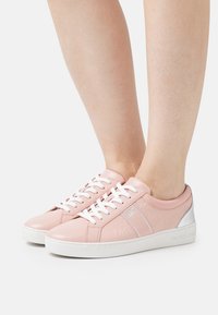 Rosa lädersneakers med vita snören och en texturerad design, med en metallisk silverdetalj vid hälen och en vit gummisula.