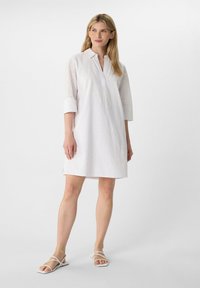 Abito in cotone bianco con colletto, maniche corte e texture a occhio di pernice. Forma dritta con spacchi laterali, abbinato a sandali bianchi.
