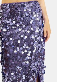 Fioletowa spódnica z cekinami, ozdobiona okrągłymi, błyszczącymi cekinami w mieszance jasnych i ciemnych odcieni. Rozcięcie po bokach dodaje wizualnego zainteresowania.