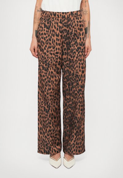 Leopardenmuster weite Hosen in Braun und Schwarz. Glattes Material, elastischer Bund, seitliche Taschen, kombiniert mit spitzen weißen Schuhen.