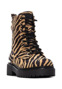 Botín de tobillo a rayas en marrón y negro con textura de ante, cordones en la parte delantera, ojales dorados, suela gruesa negra y cremallera en el lateral.