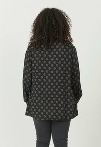 Sort skjorte med et blomsterdesign i grå og rød, med løs pasform, lange ærmer og rundet kant. Glat materiale og afslappet design.