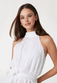 White sleeveless dress with a high neck, featuring floral embroidery, a cinched waist, and a fabric tie belt. Smooth, lightweight texture.