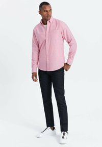 Vaaleanpunainen pitkähihainen nappipaita, jossa on tasku, yhdistettynä tummiin farkkuihin ja valkoisiin tennareihin, joissa on väriyksityiskohtia. Pehmeä tekstuuri.