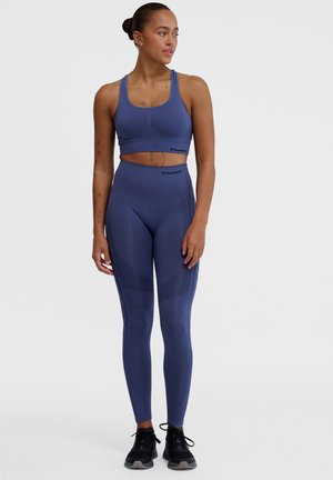 Ensemble de soutien-gorge de sport et leggings bleu marine en matériau extensible avec des accents texturés. Conception ajustée avec logo de la marque sur la ceinture.