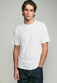 Witte katoenen t-shirt met korte mouwen, ronde hals, subtiele textuur en een ontspannen pasvorm, gecombineerd met donkere denim jeans.