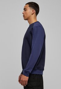 Marineblauwe trui met een ronde hals, lange mouwen en geribbelde manchetten. Gladde textuur met een contrasterend paneelontwerp op de schouders.