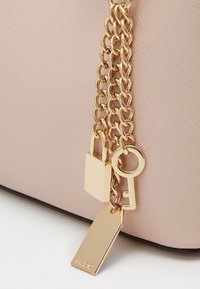 Różowa torebka o fakturowanej powierzchni z złotym łańcuszkiem, na którym zawieszono zamek, klucz i zawieszkę.