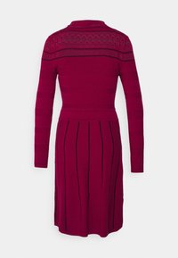 Robe bordeaux à mi-cuisses avec manches longues, présentant des motifs texturés et des rayures noires verticales. Encolure à col et corsage ajusté.