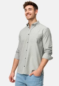 Camisa de manga larga gris claro con cuello abotonado, bolsillo en el pecho y botones verdes, llevada con jeans azul claro.
