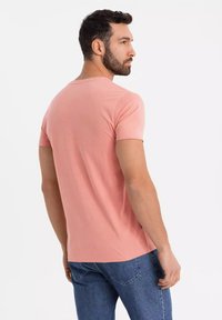 T-shirt rosa chiaro a maniche corte in tessuto morbido, con collo rotondo e vestibilità casual, abbinato a jeans in denim blu scuro.