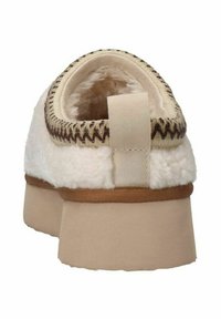 Witte pluche slof met een textuur, ronde hak, bruine stiksels en een beige stoffen lus aan de achterkant. Dikke zool.