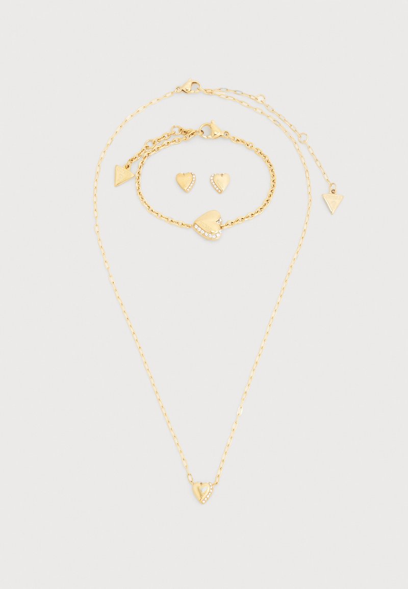 Σετ κοσμημάτων σε χρυσό τόνο που περιλαμβάνει κολιέ και βραχιόλι με κρεμαστά καρδιές, καθώς και ταιριαστά σκουλαρίκια σε σχήμα καρδιάς. Περιλαμβάνονται περίτεχνες λεπτομέρειες.