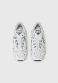 Baskets blanches de sport avec une tige en tissu texturé, des panneaux en maille et un col rembourré. Présente un logo gris sur le côté et une semelle profilée.