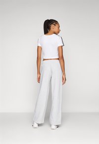 Camiseta branca cortada com riscas laterais pretas, combinada com calças de moletom largas cinza claro. Tecido macio com cintura elástica, ajuste casual.