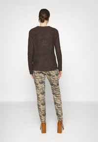 Pullover castanho de malha com mangas longas, combinado com calças camufladas em tons de bege e cinza, e sapatos de salto quadrado castanhos.