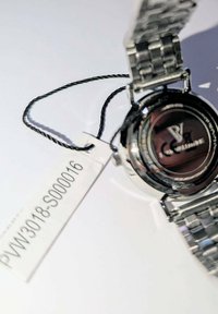 Silver metal wristwatch with a stainless steel bracelet, round black dial, and visible branding on the case back. Includes a price tag.