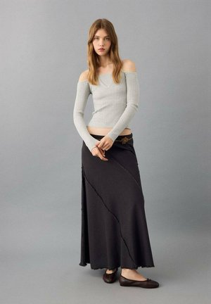 Grey ribbed off-shoulder top paired with a long black skirt featuring a wavy hem and decorative belt, finished with dark flat shoes.