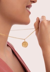 Goldkette mit einem runden Anhänger, der kunstvoll mit einem Baum-Motiv gestaltet ist. Die Kette hat ein zartes Gliederdesign.