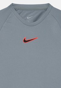 Hall ümberkaelusega hall sportlik T-särk. Rinnal on must Nike logo punase ääristusega. Tehtud sujuvast ja hingavast kangast.
